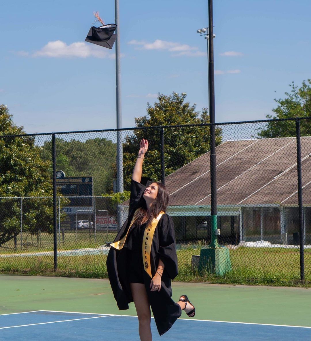 Coraline Lamer en tenue de diplômée sur un terrain de tennis
